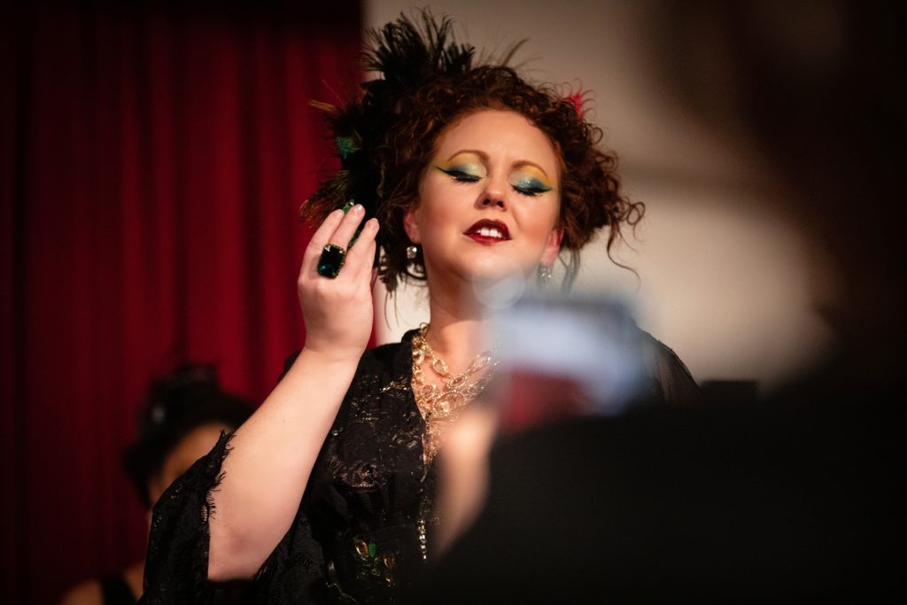 DC Burlesque performer Isabelle Epoque faces the camera with her eyes cast down smelling a perfume
